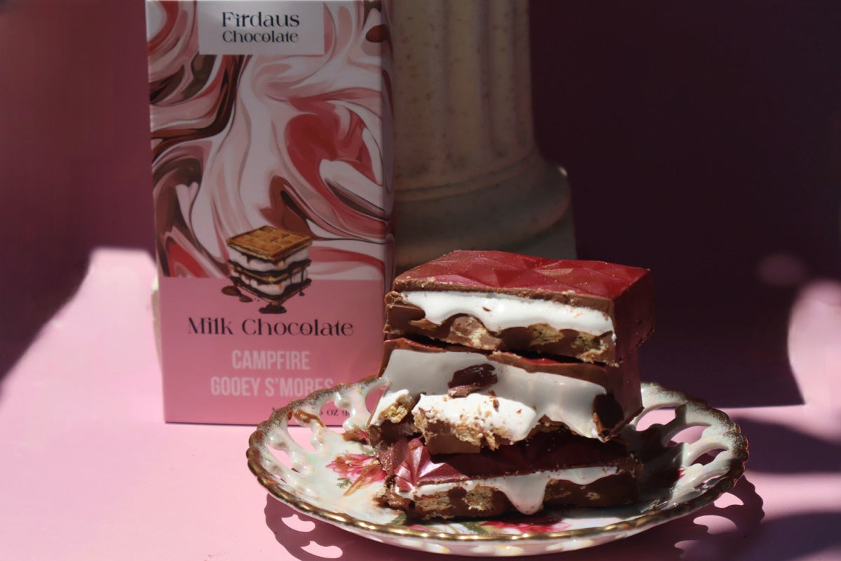 Milk chocolate campfire cookie with a box of Firdaus Chocolate in the background on a pink surface.