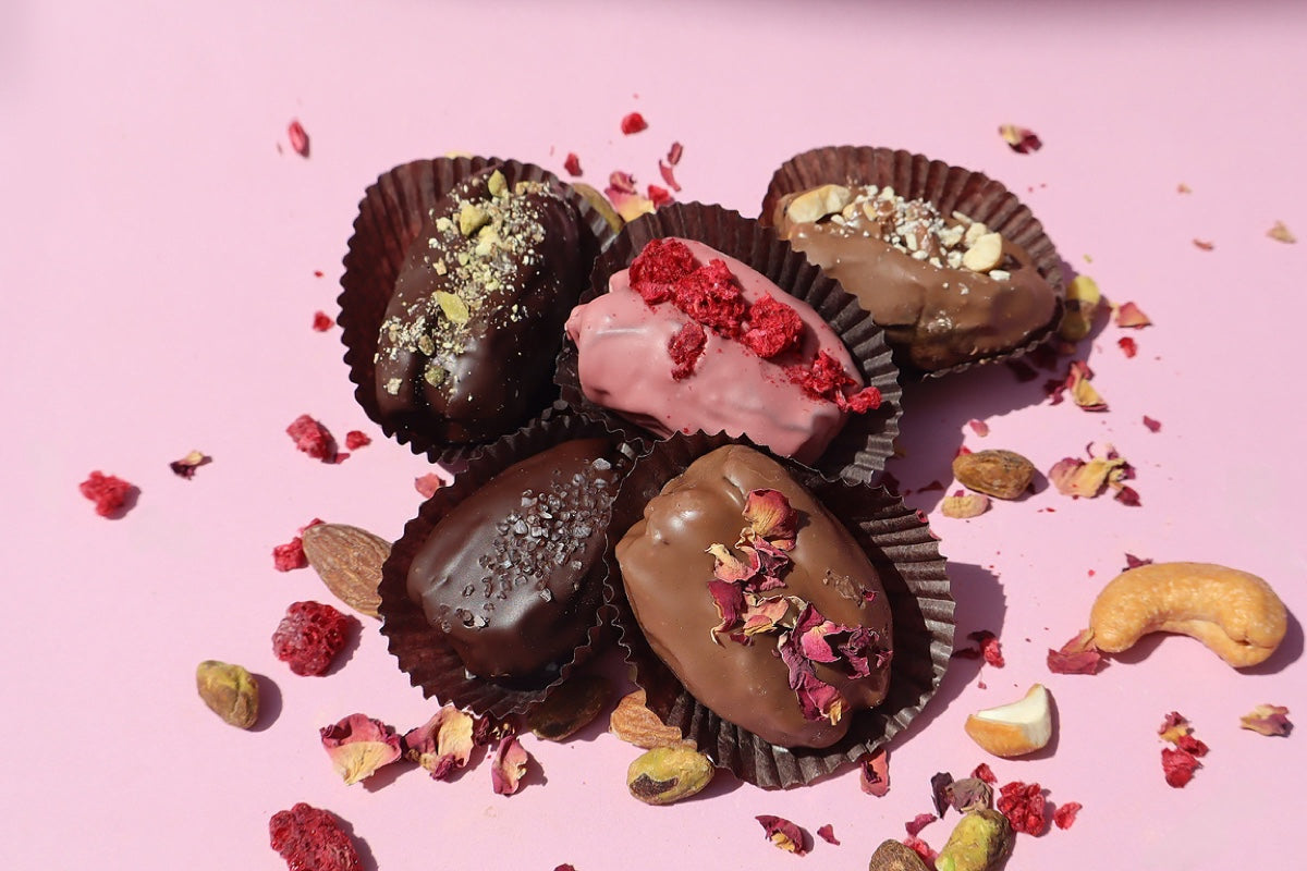 Assorted Firdaus Chocolate covered dates with glossy chocolate coating and chewy date interior on a white background.